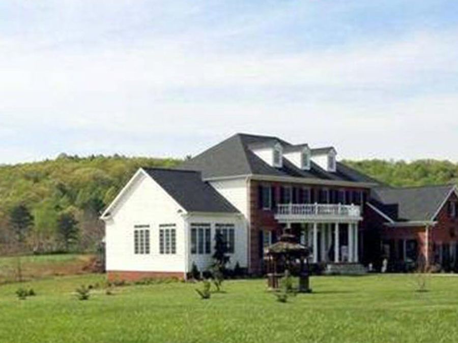 White farmhouse on a green lawn with hills behind it